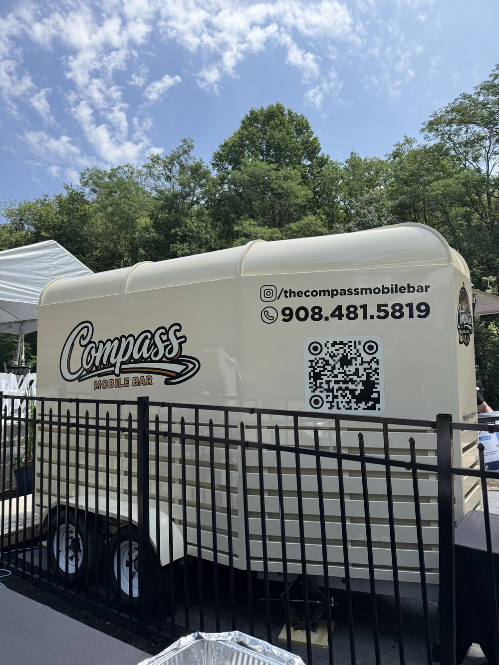 The rear panel of the Compass Mobile Bar with Instagram handle, phone number, and QR code at a backyard party