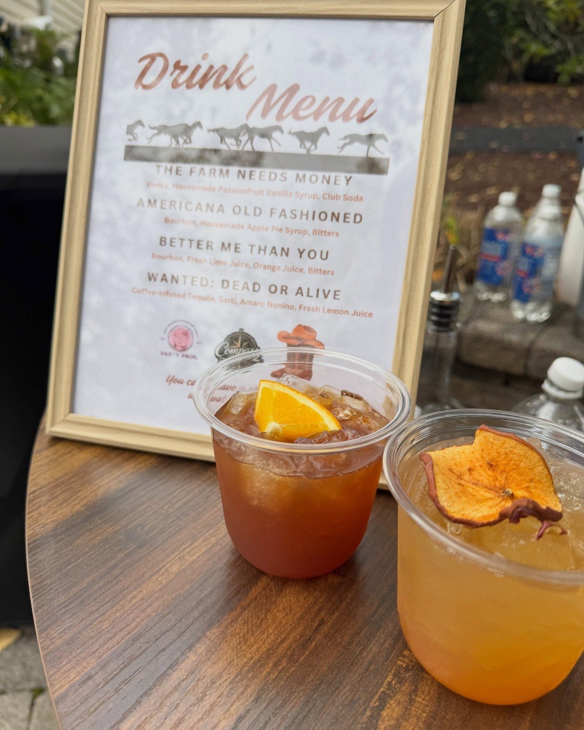 Framed Compass Mobile Bar drink menu with four race day cocktails, next to two cocktails on the wooden bar