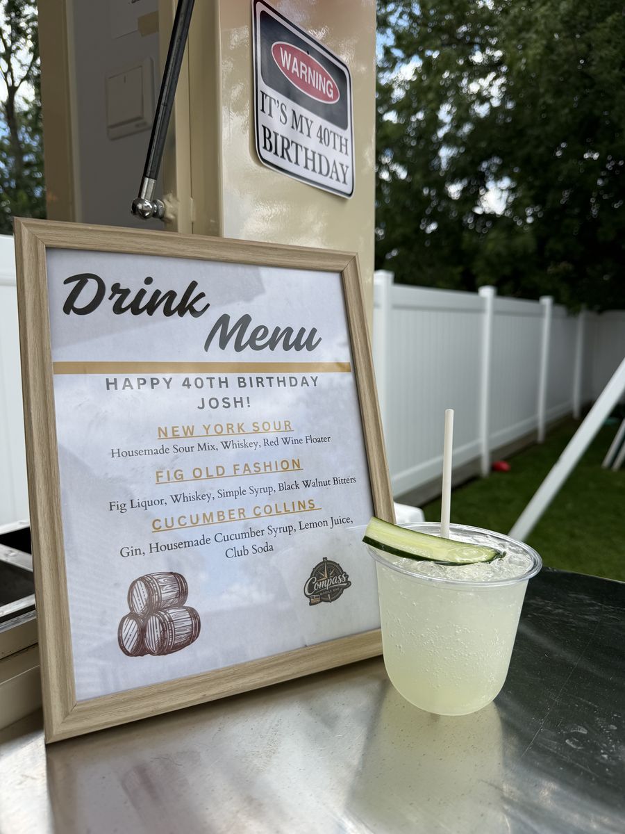 Cucumber Collins cocktail with a cucumber ribbon garnish in front of the birthday drink menu