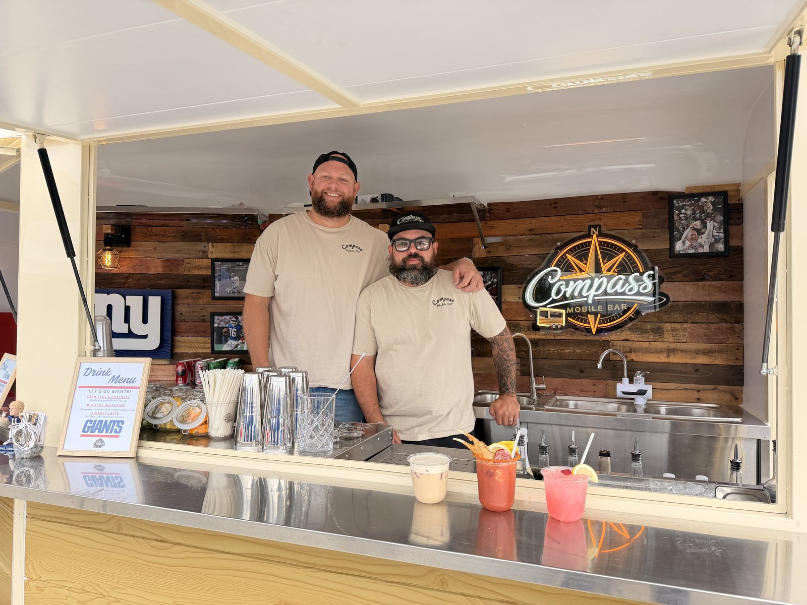 The two Compass bartenders behind the trailer bar at MetLife with the gameday drinks lined up in front of them