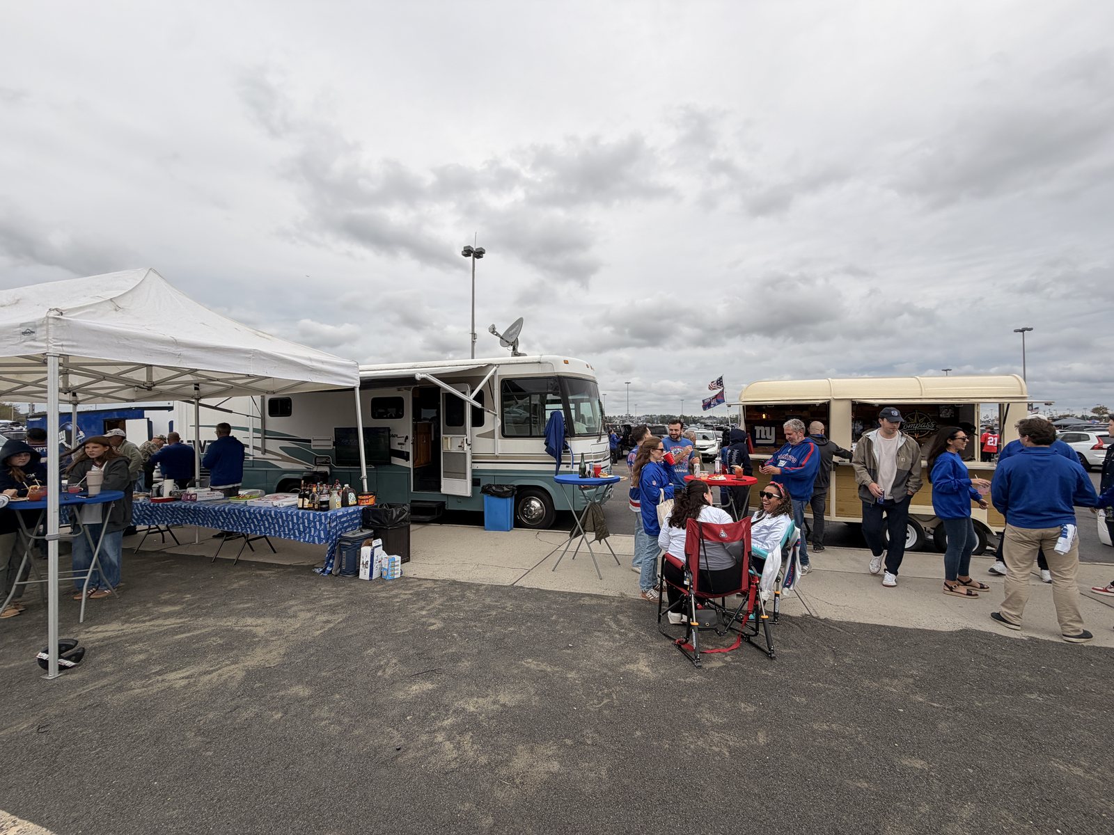 Tailgaters gathered around the Compass trailer at MetLife Stadium beside an RV and a tailgate tent