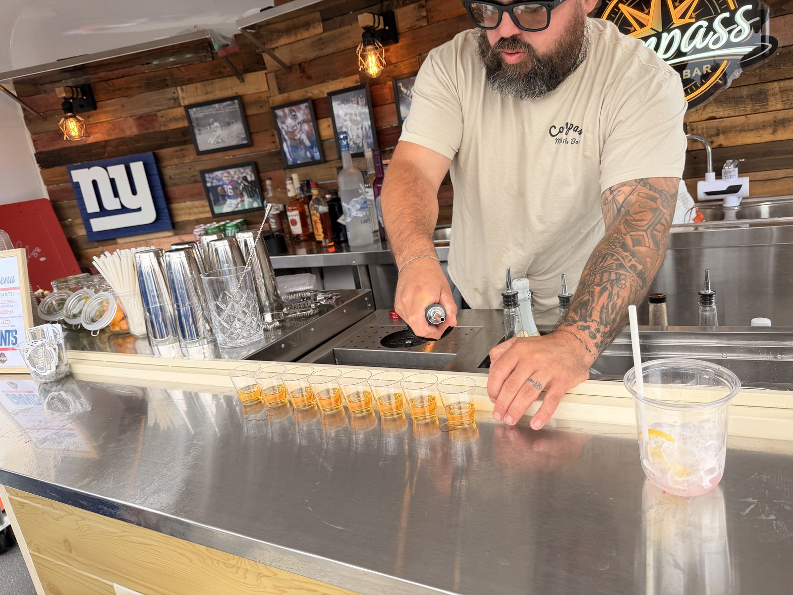 A Compass bartender pouring a row of shots along the stainless bar top