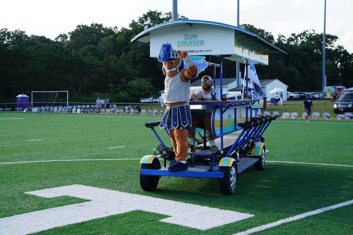The Warriors mascot riding across the turf field on the Sun Cruiser party bike at the pep rally