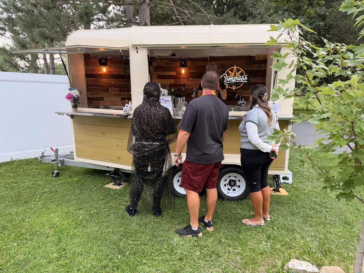 Guests in capes and a starry cloak ordering at the Compass trailer bar window